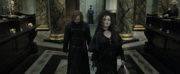 Movie still from “Harry Potter and the Deathly Hallows: Part 2” (2011), directed by David Yates – A man and a woman dressed in black walking down a hall way; Medium shot, Low angle