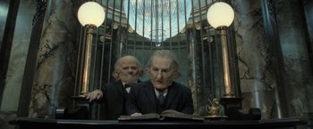 Movie still from “Harry Potter and the Deathly Hallows: Part 2” (2011), directed by David Yates – Two men in suits and ties are sitting at a desk; Medium shot, Low angle