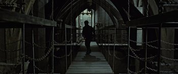 Movie still from “Harry Potter and the Deathly Hallows: Part 2” (2011), directed by David Yates – A person walking down a wooden bridge with chains; Wide shot, High angle