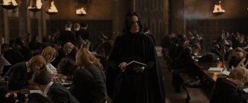Movie still from “Harry Potter and the Goblet of Fire” (2005), directed by Mike Newell – A man in a black cape holding a book in front of a crowd of onlookers; Medium shot, Over the shoulder angle