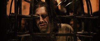 A man with long hair and a beard is looking through a fence
