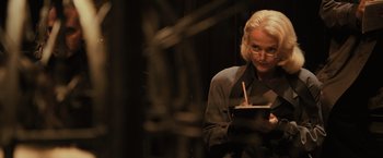 Movie still from “Harry Potter and the Goblet of Fire” (2005), directed by Mike Newell – An older woman writing on a piece of paper in a dimly - lit room; Medium shot, Over the shoulder angle
