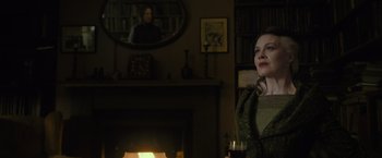 Movie still from “Harry Potter and the Half-Blood Prince” (2009), directed by David Yates – A woman sitting in front of a fireplace holding a glass of wine; Medium shot, Over the shoulder angle