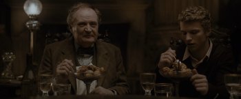 Movie still from “Harry Potter and the Half-Blood Prince” (2009), directed by David Yates – A man sitting at a table with a plate of food in front of him; Medium shot, Low angle