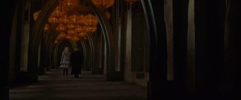 Movie still from “Harry Potter and the Half-Blood Prince” (2009), directed by David Yates – A person walking down a dark hallway with lights hanging from the ceiling; Extreme Wide shot, High angle