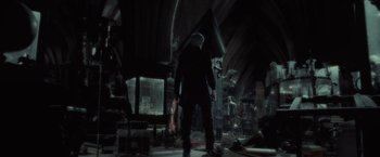Movie still from “Harry Potter and the Half-Blood Prince” (2009), directed by David Yates – A man standing in a dark room holding a violin; Wide shot, High angle