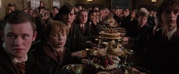 Movie still from “Harry Potter and the Order of the Phoenix” (2007), directed by David Yates – A group of people sitting at a table with cakes; Medium shot, High angle