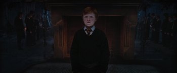 Movie still from “Harry Potter and the Order of the Phoenix” (2007), directed by David Yates – A boy in a black shirt and tie in front of a fire place; Medium shot, Low angle