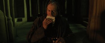 Movie still from “Harry Potter and the Order of the Phoenix” (2007), directed by David Yates – An old man sitting on the ground eating a piece of bread; Medium shot, Low angle