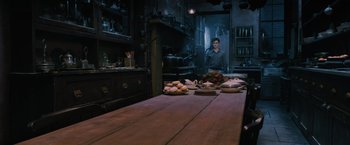 Movie still from “Harry Potter and the Order of the Phoenix” (2007), directed by David Yates – A man standing in front of a wooden table with food on it; Wide shot, High angle