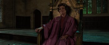 Movie still from “Harry Potter and the Order of the Phoenix” (2007), directed by David Yates – An older woman sitting on a chair in front of a wall; Medium shot, Low angle