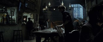 Movie still from “Harry Potter and the Prisoner of Azkaban” (2004), directed by Alfonso Cuarón – A man cutting paper with a knife in a dark room; Wide shot, High angle