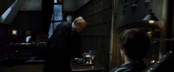 Movie still from “Harry Potter and the Prisoner of Azkaban” (2004), directed by Alfonso Cuarón – A man standing in front of a pan of food on top of a table; Medium shot, Over the shoulder angle