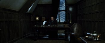 Movie still from “Harry Potter and the Prisoner of Azkaban” (2004), directed by Alfonso Cuarón – A man sitting at a desk in a dark room; Wide shot, High angle