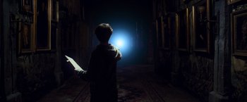 Movie still from “Harry Potter and the Prisoner of Azkaban” (2004), directed by Alfonso Cuarón – A boy standing in a dark room holding a book; Wide shot, Low angle