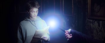 Movie still from “Harry Potter and the Prisoner of Azkaban” (2004), directed by Alfonso Cuarón – A young man reading a paper while holding a wand; Medium shot, Over the shoulder angle