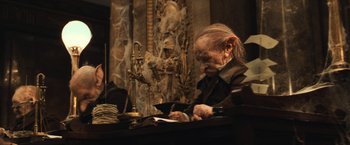 Movie still from “Harry Potter and the Sorcerer's Stone” (2001), directed by Chris Columbus – An old man sitting at a table reading a book; Medium shot, Low angle