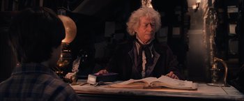 Movie still from “Harry Potter and the Sorcerer's Stone” (2001), directed by Chris Columbus – An old man sitting at a table reading a book; Medium shot, Over the shoulder angle