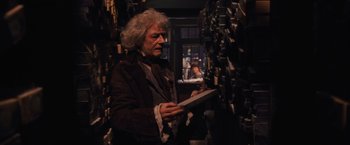 Movie still from “Harry Potter and the Sorcerer's Stone” (2001), directed by Chris Columbus – An older man is holding a book in a library; Medium shot, Low angle