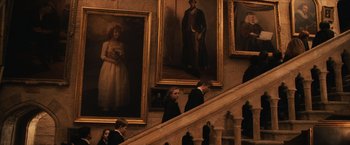 Movie still from “Harry Potter and the Sorcerer's Stone” (2001), directed by Chris Columbus – A group of people walking up the stairs in front of a wall of paintings; Wide shot, Low angle