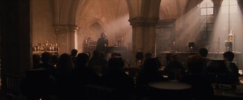 Movie still from “Harry Potter and the Sorcerer's Stone” (2001), directed by Chris Columbus – A man is giving a lecture to a group of people; Wide shot, Over the shoulder angle