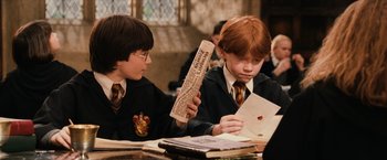 Movie still from “Harry Potter and the Sorcerer's Stone” (2001), directed by Chris Columbus – Two young boys sitting at a table with a piece of paper in front of them; Medium shot, High angle