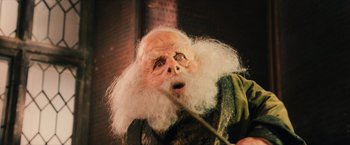 Movie still from “Harry Potter and the Sorcerer's Stone” (2001), directed by Chris Columbus – An old man with a white beard is holding something in his mouth; Close Up shot, Low angle