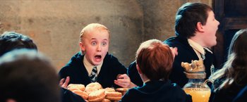 Movie still from “Harry Potter and the Sorcerer's Stone” (2001), directed by Chris Columbus – A young boy in a school uniform looking surprised at a table full of doughnuts; Medium shot, Over the shoulder angle
