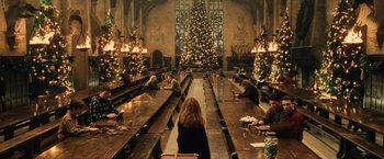 Movie still from “Harry Potter and the Sorcerer's Stone” (2001), directed by Chris Columbus – People sitting at long wooden tables in front of a christmas tree; Extreme Wide shot, High angle