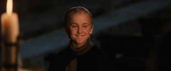 Movie still from “Harry Potter and the Sorcerer's Stone” (2001), directed by Chris Columbus – A young man smiling for the camera in a dark room; Close Up shot, Low angle