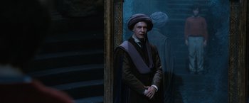 Movie still from “Harry Potter and the Sorcerer's Stone” (2001), directed by Chris Columbus – A man wearing a purple hat standing in front of a painting; Medium shot, Over the shoulder angle