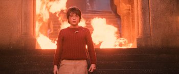 Movie still from “Harry Potter and the Sorcerer's Stone” (2001), directed by Chris Columbus – A boy in a red sweater standing in front of a fire; Medium shot, High angle