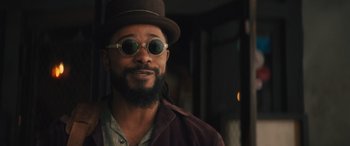 Movie still from “Haunted Mansion” (2023), directed by Justin Simien – A man with a beard wearing sunglasses and a hat; Close Up shot, Low angle