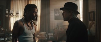 Movie still from “Haunted Mansion” (2023), directed by Justin Simien – A man in a hat and a man with dreadlocks talking to each other in a room; Medium shot, Over the shoulder angle