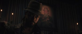 Movie still from “Haunted Mansion” (2023), directed by Justin Simien – A person wearing a hat with a painting in the background; Close Up shot, Low angle