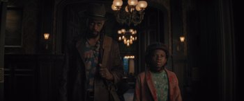 Movie still from “Haunted Mansion” (2023), directed by Justin Simien – A man standing next to a young boy in a room; Medium shot, Low angle