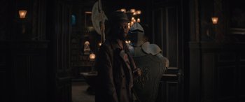 Movie still from “Haunted Mansion” (2023), directed by Justin Simien – A man standing in front of a wall with a shield; Medium shot, Over the shoulder angle