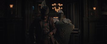 Movie still from “Haunted Mansion” (2023), directed by Justin Simien – A man standing next to an armored man in a dark room; Medium shot, Low angle