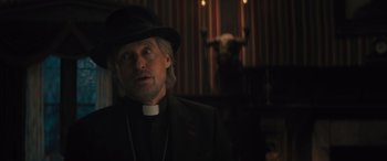 Movie still from “Haunted Mansion” (2023), directed by Justin Simien – A man wearing a priest's outfit and a black hat; Close Up shot, Over the shoulder angle