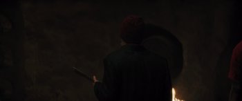 Movie still from “Haunted Mansion” (2023), directed by Justin Simien – A man in a black jacket and a red hat holding a knife; Medium shot, Over the shoulder angle