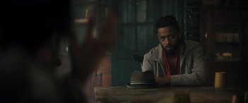 Movie still from “Haunted Mansion” (2023), directed by Justin Simien – A man sitting at a wooden table with a hat on; Close Up shot, Over the shoulder angle