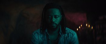 Movie still from “Haunted Mansion” (2023), directed by Justin Simien – A man with dreadlocks sitting in a dark room; Close Up shot, Overhead angle