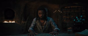 Movie still from “Haunted Mansion” (2023), directed by Justin Simien – A man sitting at a table in front of candles; Medium shot, Low angle