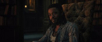 Movie still from “Haunted Mansion” (2023), directed by Justin Simien – A man sitting in a chair in a living room; Close Up shot, Over the shoulder angle