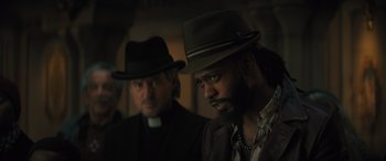 Movie still from “Haunted Mansion” (2023), directed by Justin Simien – Two men in hats and suits are standing together; Close Up shot, Over the shoulder angle