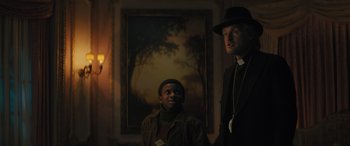 Movie still from “Haunted Mansion” (2023), directed by Justin Simien – A man and a young boy standing in front of a painting; Medium shot, Low angle