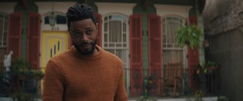 Movie still from “Haunted Mansion” (2023), directed by Justin Simien – A man in a sweater standing in front of a building; Close Up shot, Over the shoulder angle