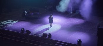 Movie still from “Hawa” (2022), directed by Maïmouna Doucouré – A woman standing on a stage with a microphone in her hand; Extreme Wide shot, Overhead angle