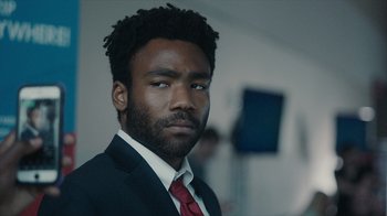 Movie still from “Atlanta” (2016), created by Donald Glover – A man in a suit and red neck tie; Close Up shot, Over the shoulder angle