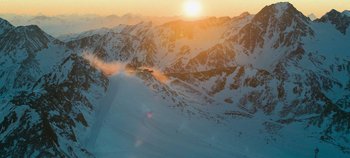 Movie still from “Heart of Stone” (2023), directed by Tom Harper – The sun is setting over a mountain range; Extreme Wide shot, High angle